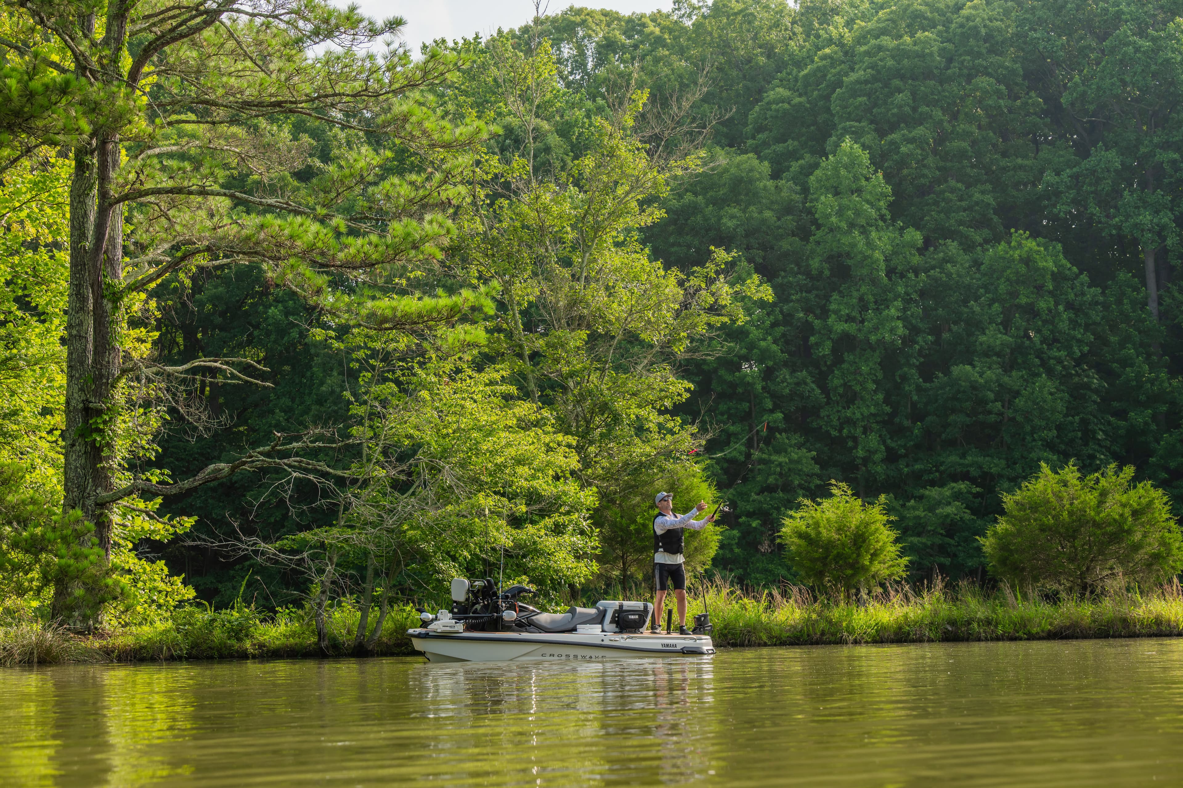 White bass boat with angler fishing on calm water surrounded by green trees