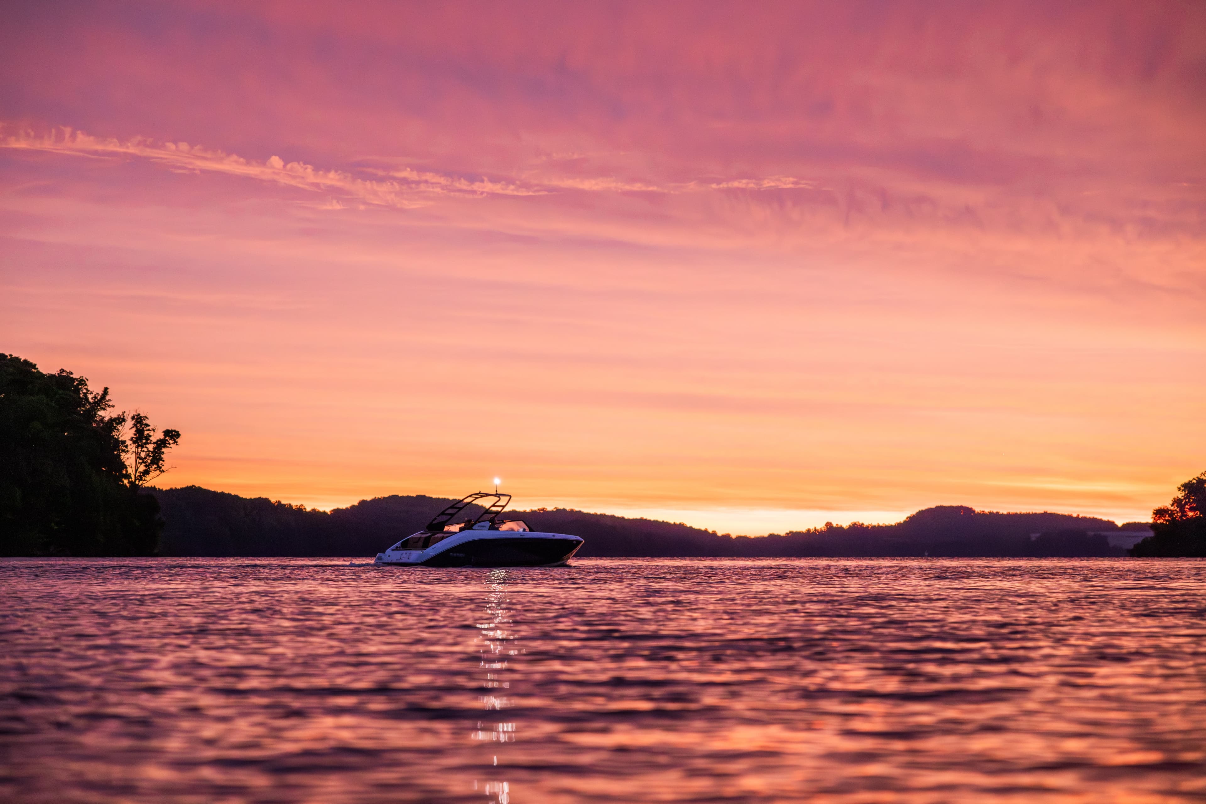 Peaceful sunset over a lake with golden reflections on calm water and hills silhouetted in the background.