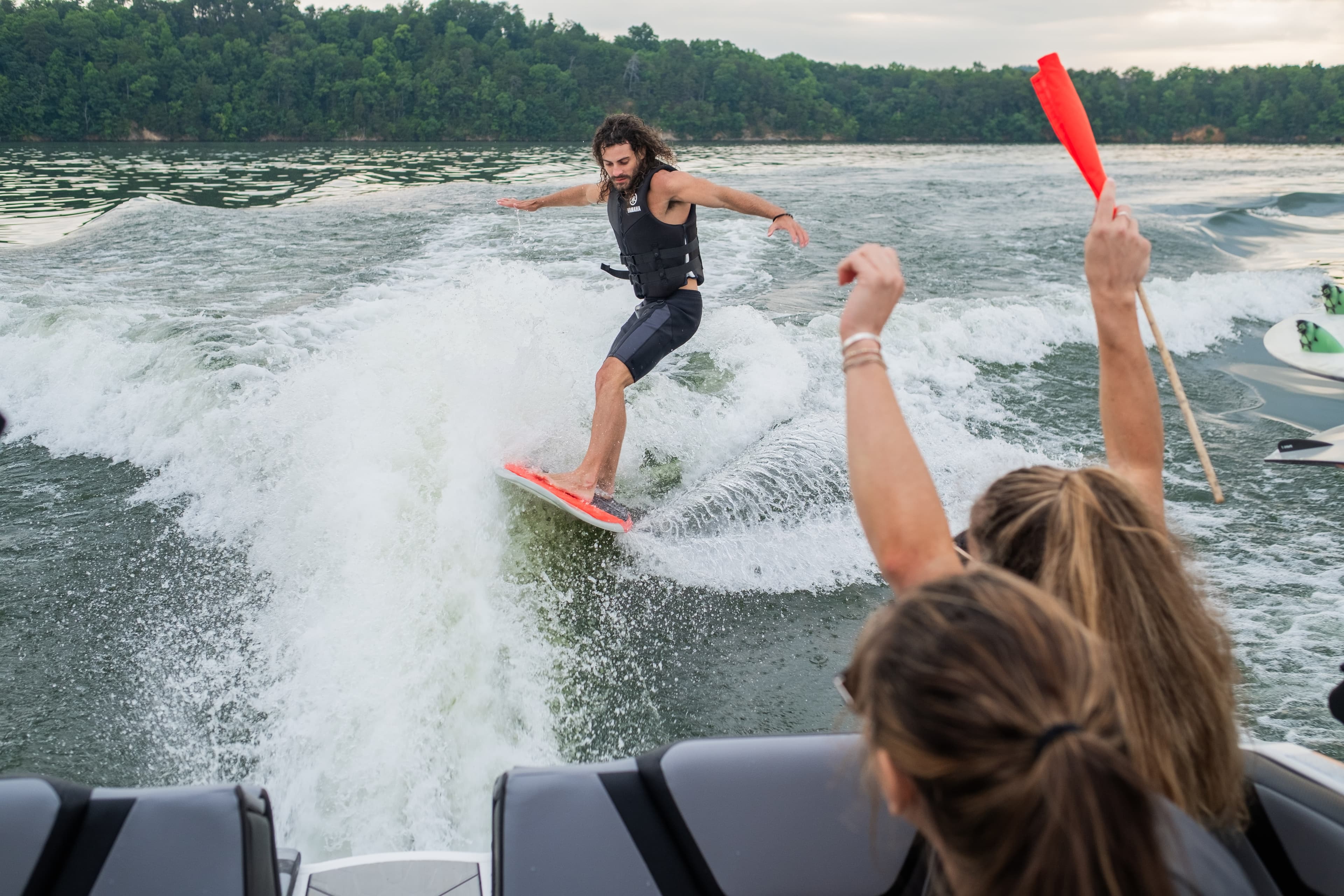Wake boat creating surf wave with wakesurfer riding while passengers watch from boat