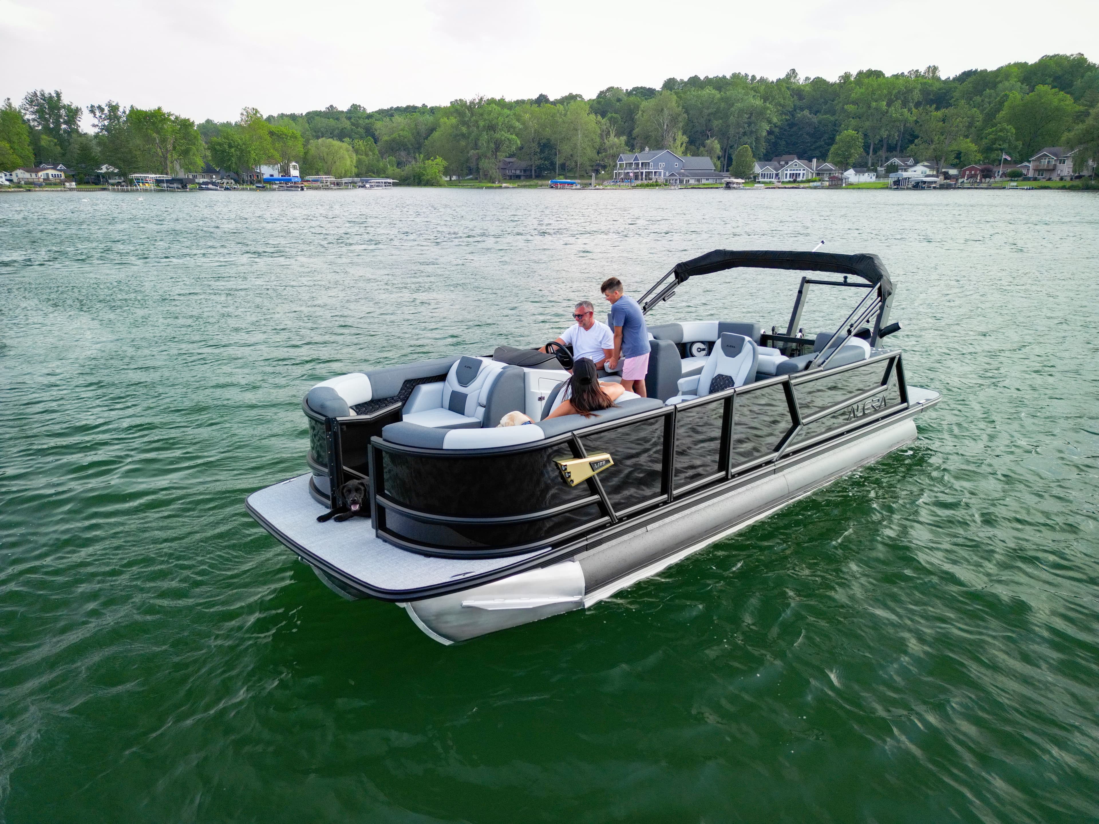 Alera Model M pontoon boat on a lake with passengers and waterfront homes in the background