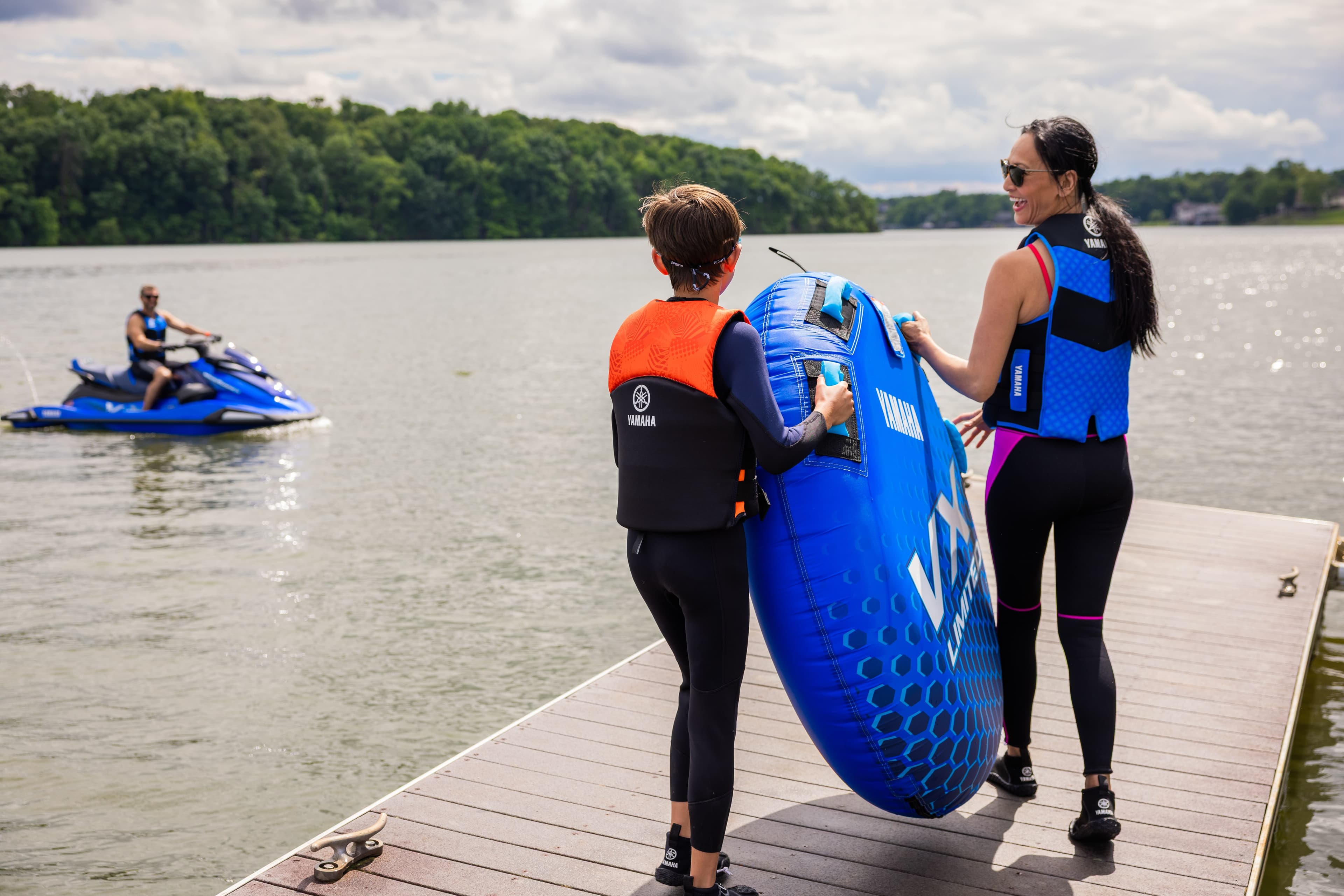 Two people on a dock with water sports equipment and a Yamaha jet ski in the background on a lake
