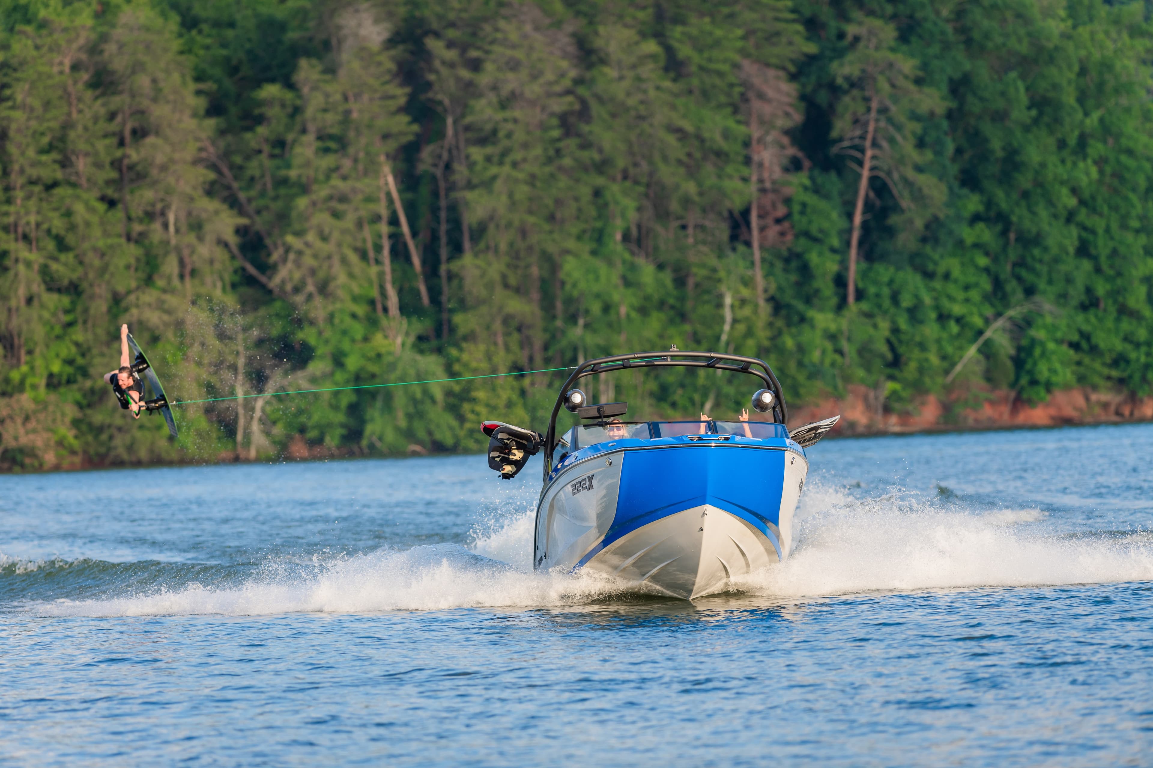 Wakeboarder performing an aerial jump behind a wakeboard boat on a lake