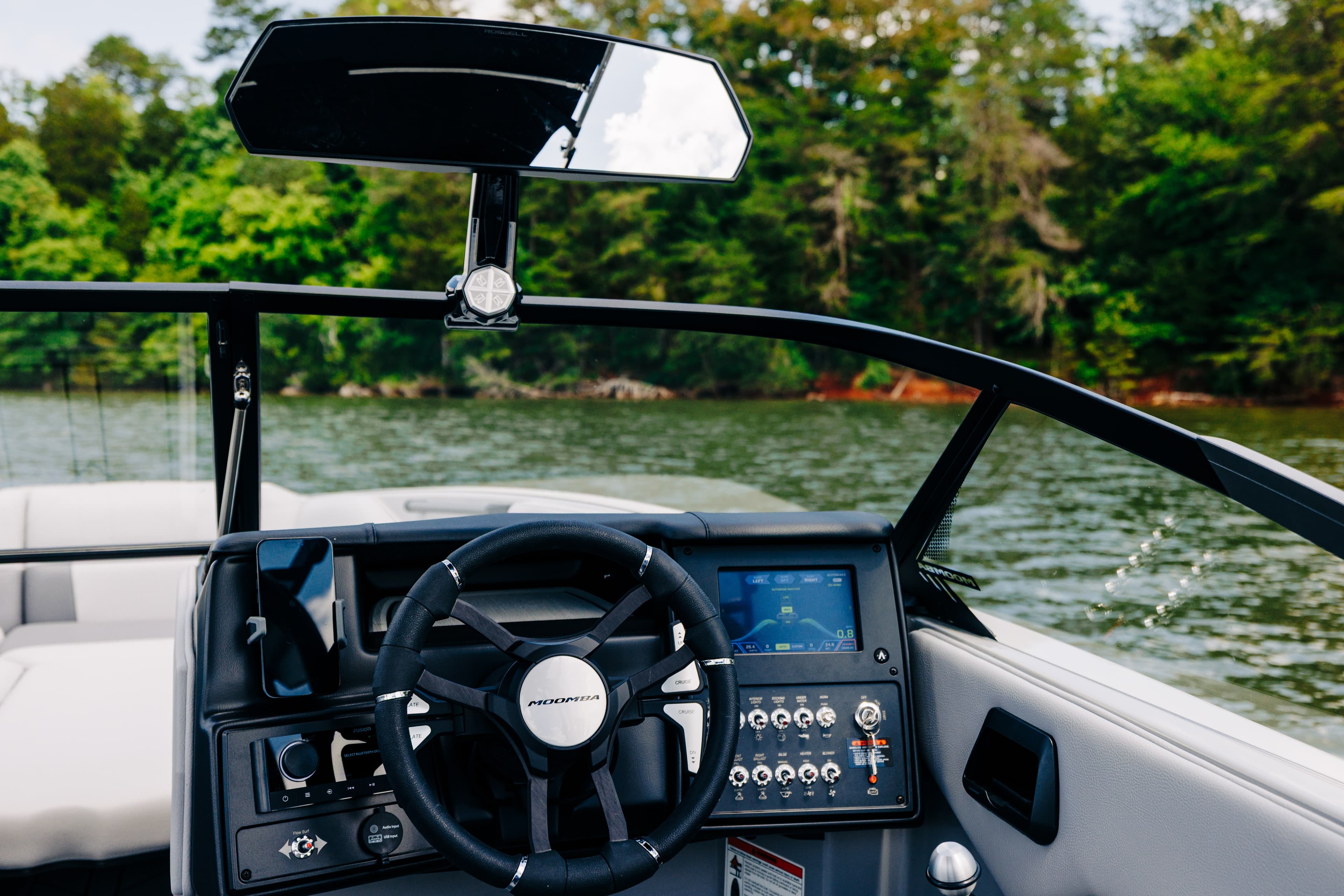 Helm station interior of a Moomba wakeboard boat on water with steering wheel, digital gauges, and control panel visible.