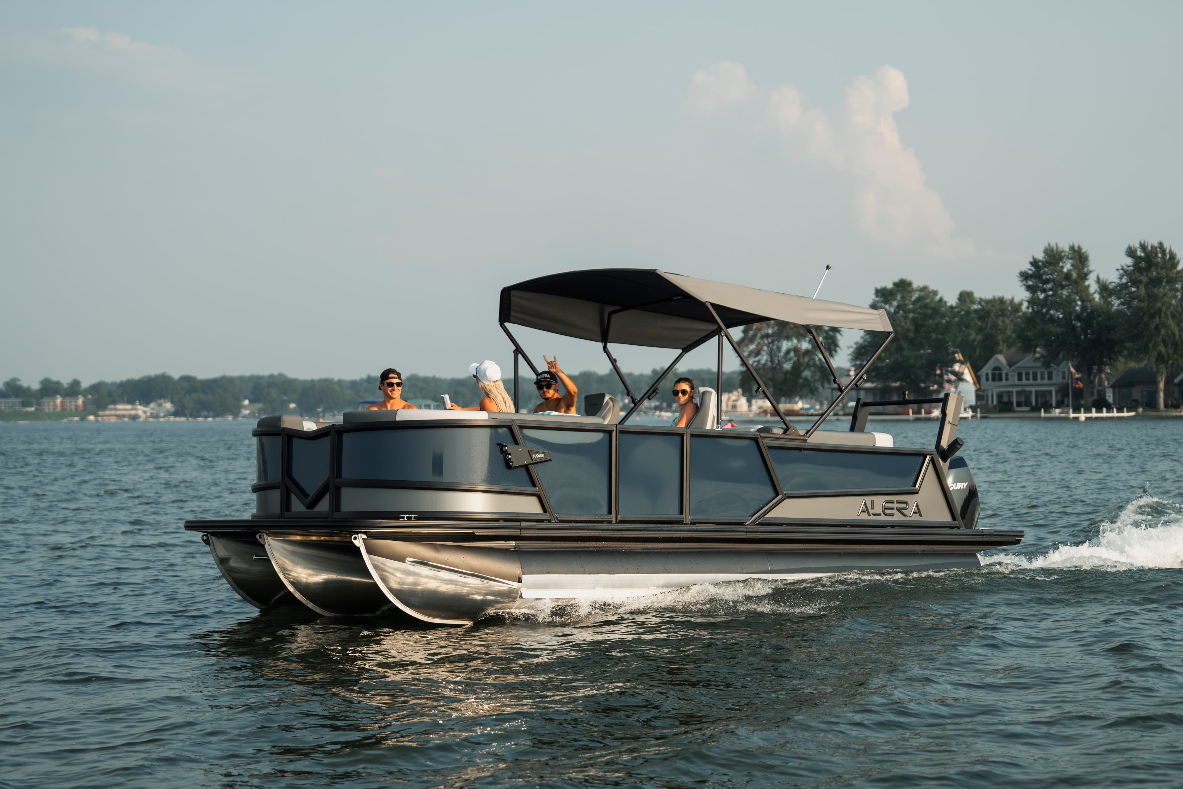Alera Model M pontoon boat cruising on a lake with passengers under a bimini top