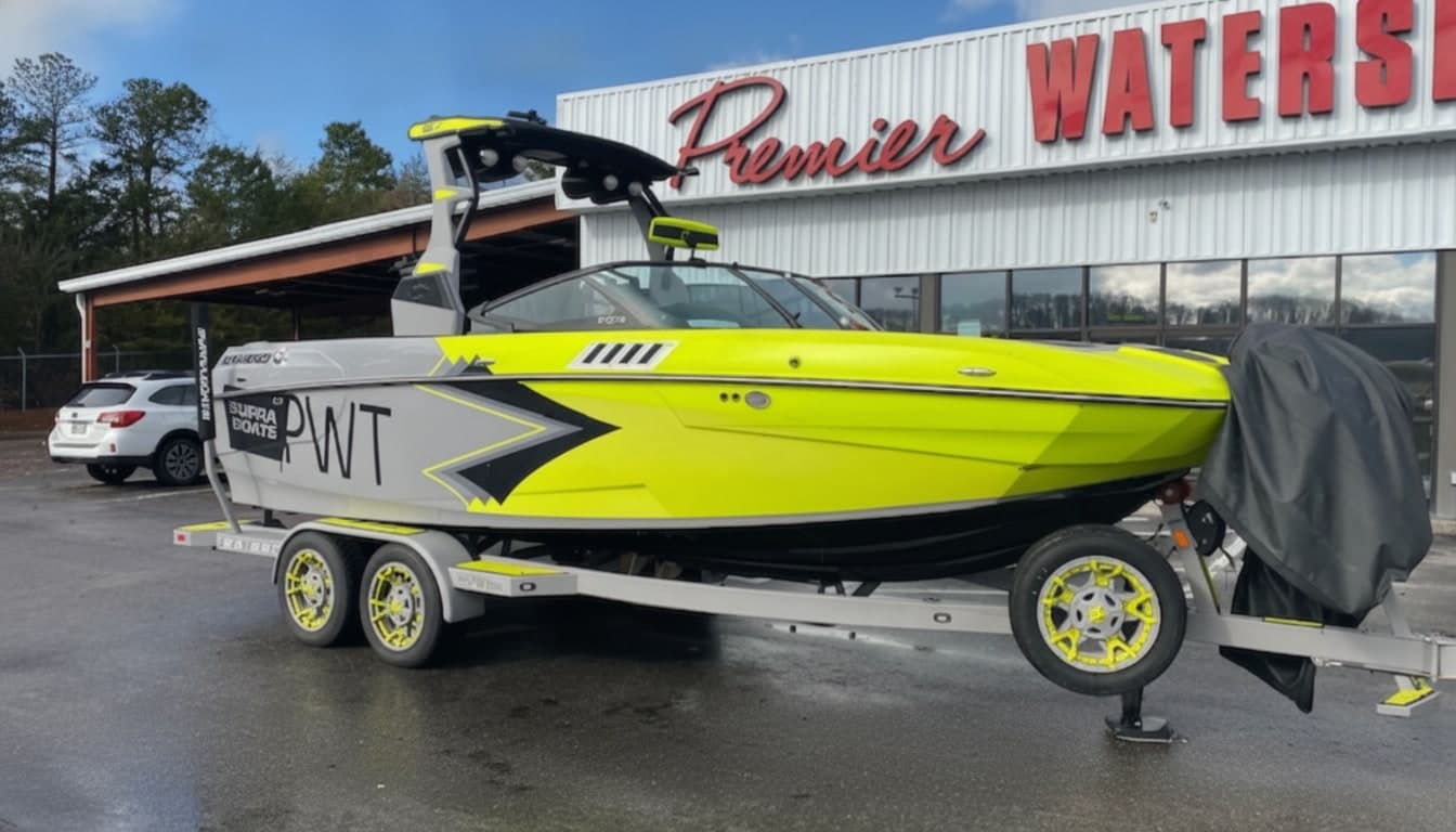 Neon yellow Supra wakeboard boat with wakeboard tower on a white and yellow trailer at Premier Watersports dealership.