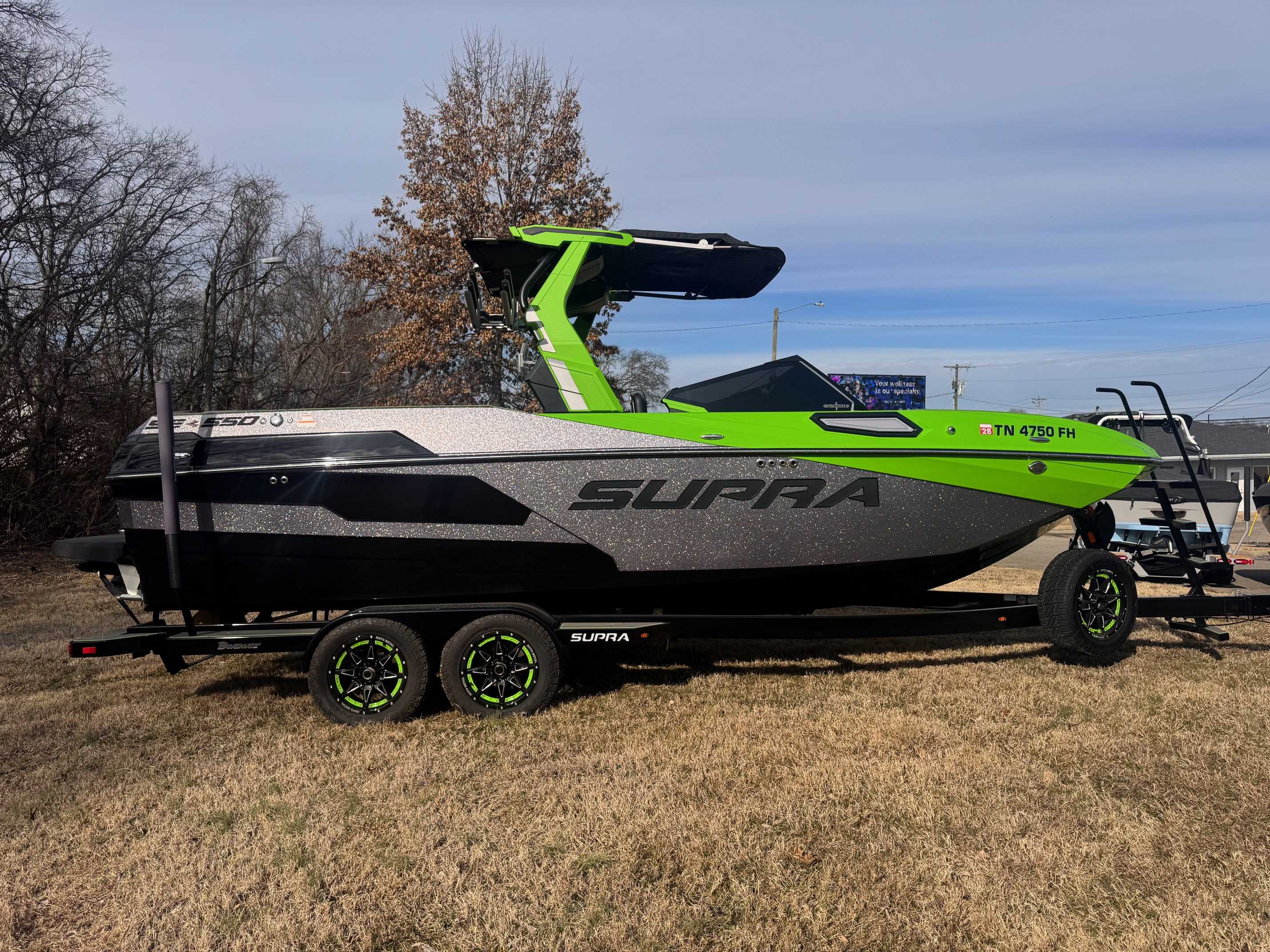Green and black Supra wakeboard boat with wake tower displayed on trailer at dealership lot