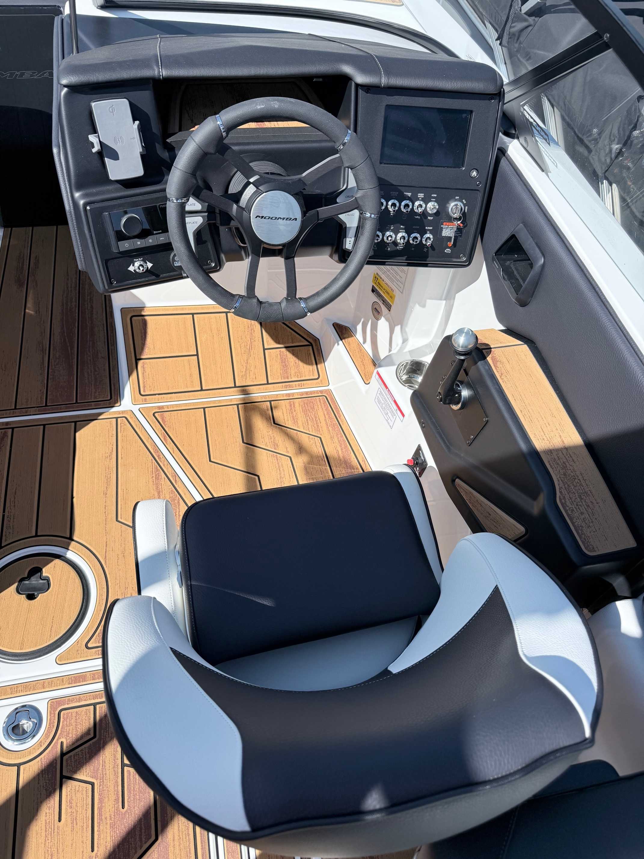 Interior view of boat cockpit showing captain's chair, helm station with steering wheel and digital controls, synthetic teak flooring